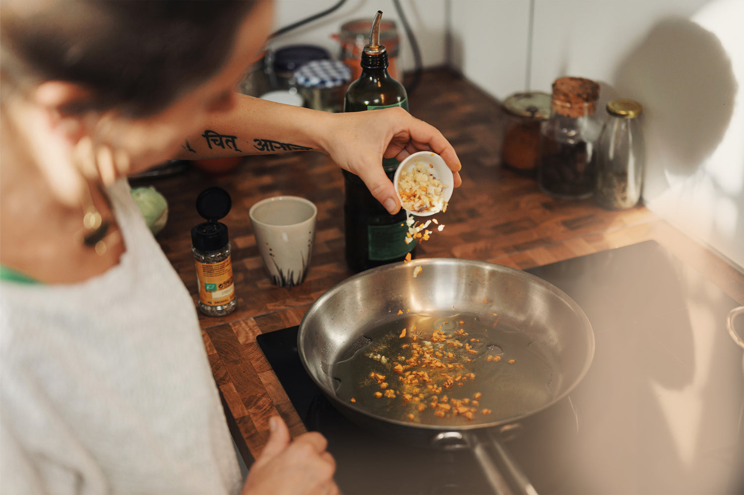 a female hobby cook adding spices to a pan in the kitchen. Olive oil and other ingredients are in the background of the kitchen sideboard